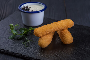 Deep-fried cheese sticks with garlic sauce on a black tray