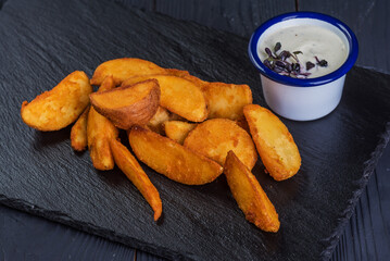Rustic deep fried potatoes with garlic sauce on a black tray