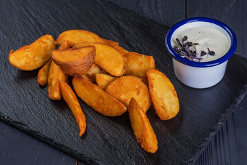 Rustic deep fried potatoes with garlic sauce on a black tray