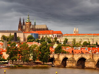 Obraz premium Prague castle, st. Vitus catedral and charles bridge in sunny day, dark dramatic stormy clouds behind. Prague historic city center. Landscape of famous prague old town, Czech Republic capital.