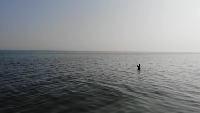 Luftaufnahme von Angler mit Angel in Wathose im Wasser bei Sonne watend per Drohne gefilmt als Fahrt