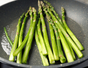 green asparagus fried in oil in a gray frying pan.  vegetarianism.  healthy food