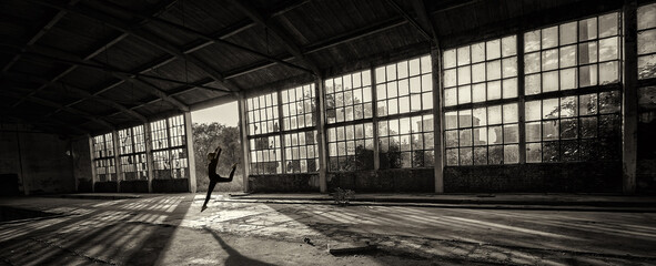 Silhouette of ballerina jumping and dancing in abandoned building on a sunny summer day 