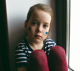 the face of a little girl, a crying child, flowing tears painted on her cheek in the yellow-blue...