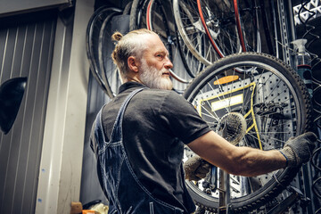 Aged mechanic fixing bicycle wheel in modern workshop