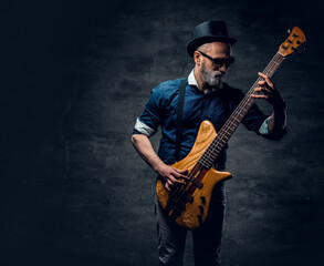 Obraz premium Cool elderly hipster guitarist playing guitar against dark background