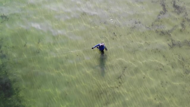 Luftaufnahme von Angler mit Angel in Wathose im Wasser bei Sonne watend per Drohne gefilmt von oben