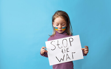 Portrait of a little girl with a painted Ukrainian flag on her face, standing on a blue background and holding a poster with the inscription Stop the war.
