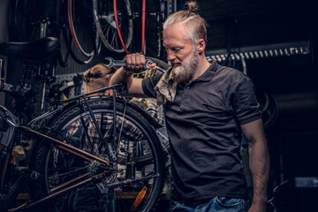 Fototapeta na wymiar Aged professional repairman posing around bicycle wheel in workshop