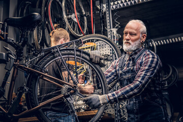 Old man and his grandson fixing bicycles together in repair shop