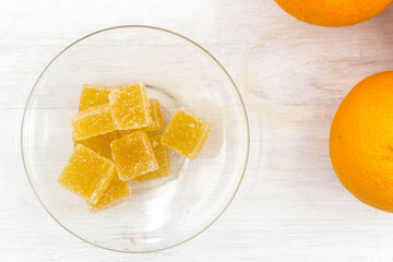 Orange marmalade candy and oranges fruits on a white wooden table.