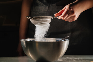 powdered sugar or flour is sifted into a bowl on a black background. 