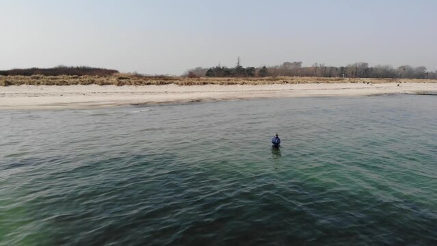 Luftaufnahme von Angler mit Angel in Wathose im Wasser bei Sonne watend per Drohne gefilmt als Schwenk