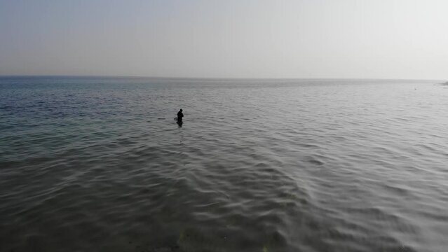 Luftaufnahme von Angler mit Angel in Wathose im Wasser bei Sonne watend per Drohne gefilmt als Fahrt