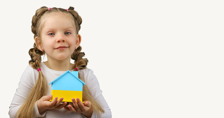 The little girl calls to Stop war, holding wooden house model in the colors of the flag of Ukraine. Grey background. Copy Space. No war. Stop war.