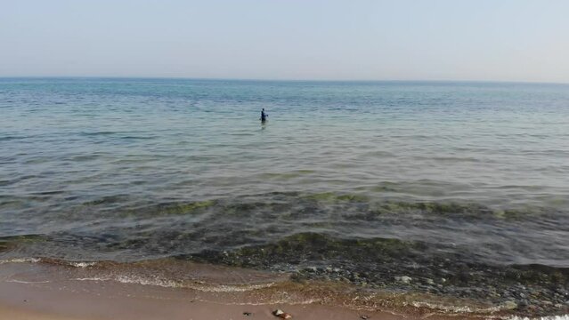 Luftaufnahme von Angler mit Angel in Wathose im Wasser bei Sonne watend per Drohne als Fahrt gefilmt