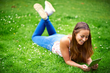 Stumbling upon some great websites. Shot of a young woman using her digital tablet while lying on the grass at the park.