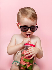 Boy in sunglasses enjoys drinking a cocktail with watermelon and mint. Posing on a pink background