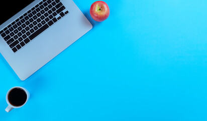 Blue office desk table with laptop computer plus apple snack and coffee. Top view with copy space...