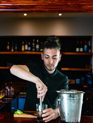 young and modern waiter, crushing the mojito ingredients to release their juices . vertical