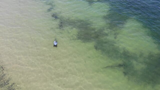 Luftaufnahme von Angler mit Angel in Wathose im Wasser bei Sonne watend per Drohne mit Schwenk gefilmt
