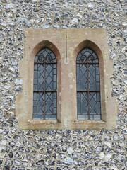 Two windows close together with bars on the stone wall of the church