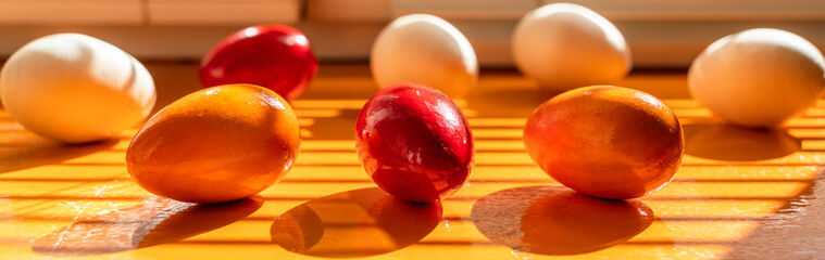 Red, orange and white wooden eggs on an orange windowsill in oblique sunlight. Minimalistic happy easter banner