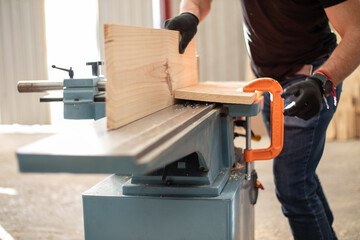 hands of a young carpenter working on an Electric Benchtop Jointer machine cutting a wooden board...