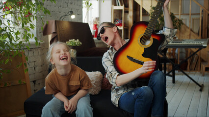 Woman entertains her daughter with guitar playing while pretending to be a rocker