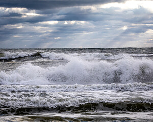 Waves breaking on beach with light rays breaking through storm clouds