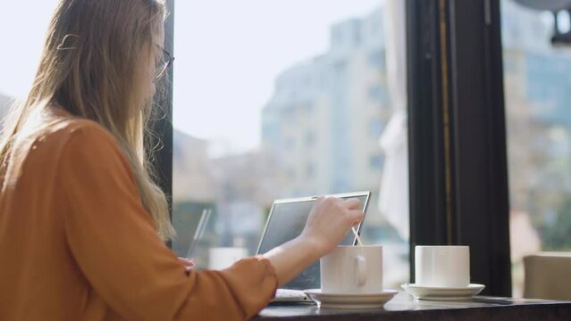 Young businesswoman in a cafe bar or restaurant. Freelancer girl working on laptop and having coffee at a window table..