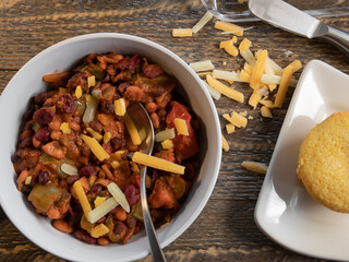 Bowl of vegetarian chilli with cornbread top view on a natural wood table