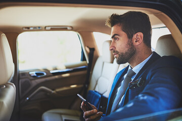 His mind is constantly on work. Shot of a focused young businessman using his cellphone and contemplating while being seated in the back of a car.