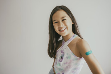 Mixed Asian preteen girl showing her arm with bandage after got vaccinated or inoculation, child...