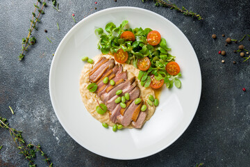 Sliced Duck breast with vegetables and risotto top view
