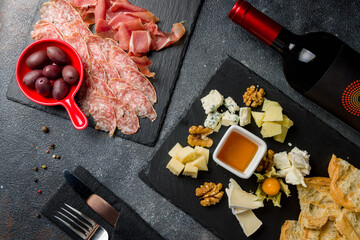 slicing of different meat and different types of european cheese on dark stone plate with olives and honey top view with red and white wine