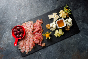 Obraz na płótnie Canvas slicing of different meat and different types of european cheese on dark stone plate with olives and honey top view