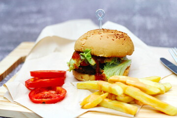 Home made hamburgers served with french fries and tomatoes on a wooden table. Fast food and junk food.