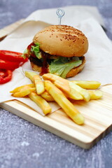 Home made hamburgers served with french fries and tomatoes on a wooden table. Fast food and junk food.