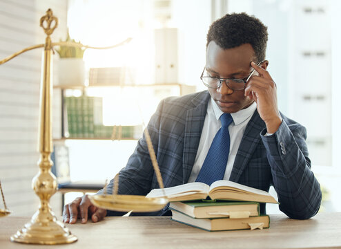 Reading Up On An Important Case. Shot Of A Young Male Lawyer Reading A Book At Work.