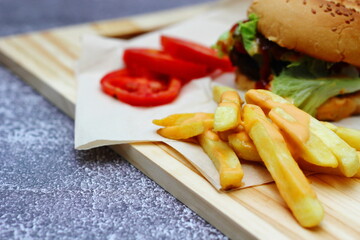 Home made hamburgers served with french fries and tomatoes on a wooden table. Fast food and junk food.