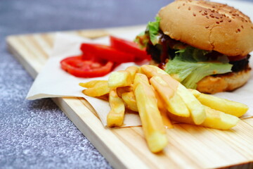Home made hamburgers served with french fries and tomatoes on a wooden table. Fast food and junk food.
