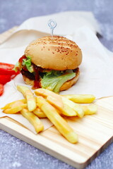 Home made hamburgers served with french fries and tomatoes on a wooden table. Fast food and junk food.