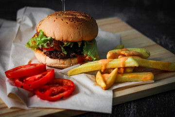 Burgers, french fries, red tomatoes served on a gray table.