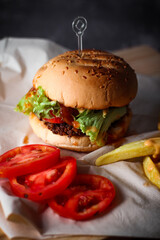 Burgers, french fries, red tomatoes served on a gray table.