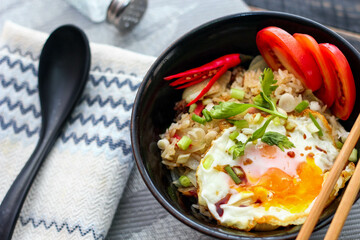 Japanese-style fried rice served in a black bowl with a fried egg and red tomato slices.