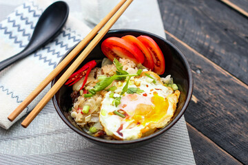 Japanese-style fried rice served in a black bowl with a fried egg and red tomato slices.