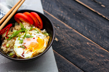 Japanese-style fried rice served in a black bowl with a fried egg and red tomato slices.