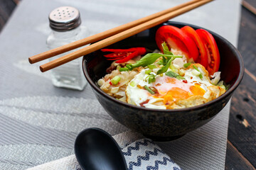 Japanese-style fried rice served in a black bowl with a fried egg and red tomato slices.