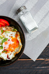 Japanese-style fried rice served in a black bowl with a fried egg and red tomato slices.